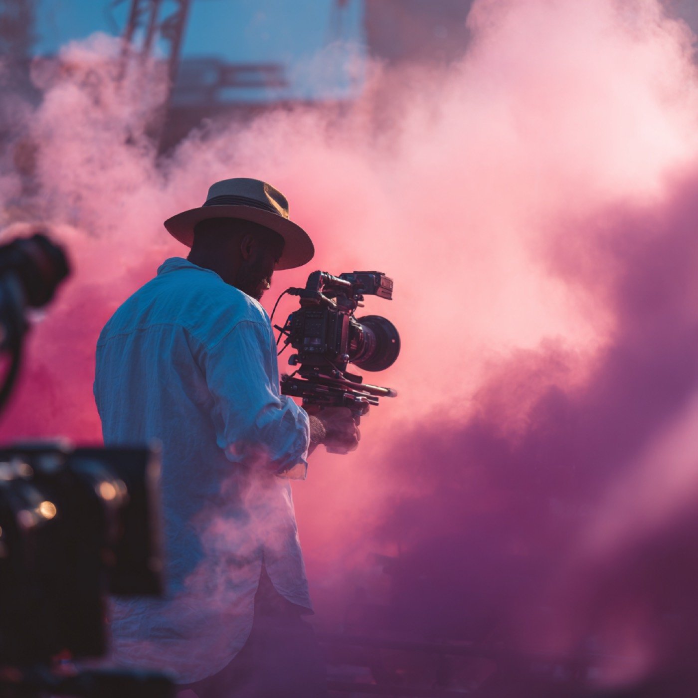 A camera operator in a wide-brimmed hat working through smoke